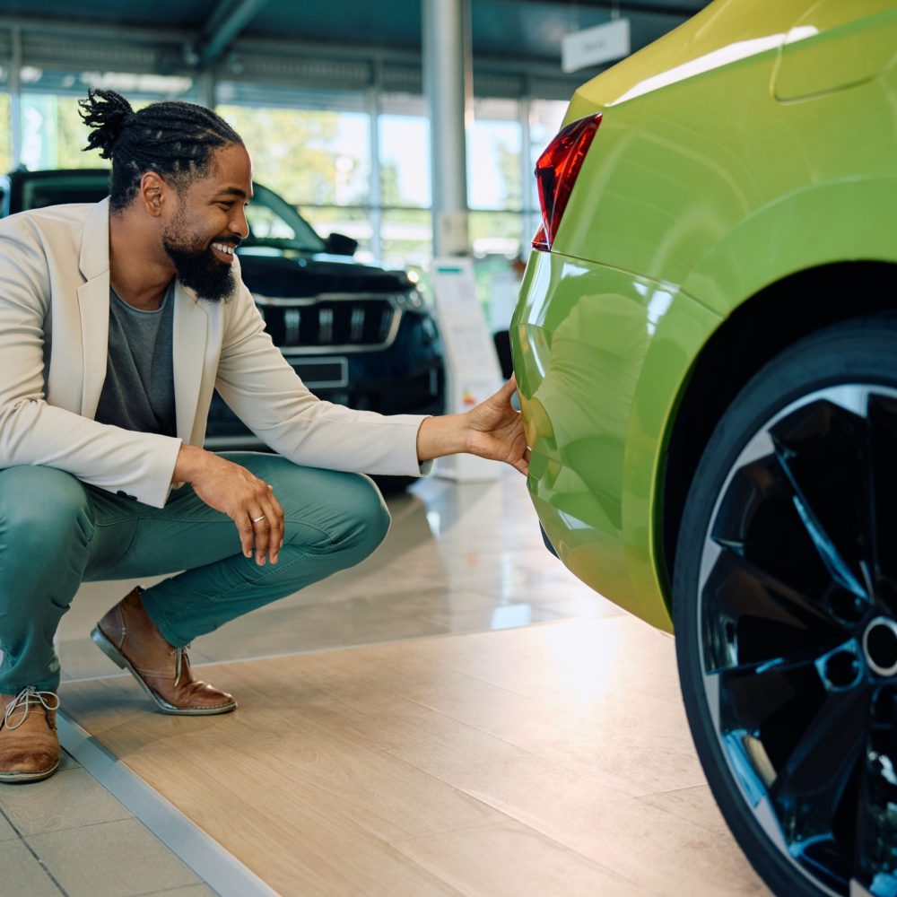 Happy African American man buying new car in auto salon.